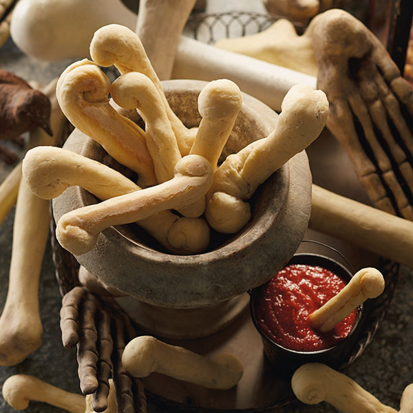 Halloween bone breadsticks in a bowl next to a dish of marinara sauce.