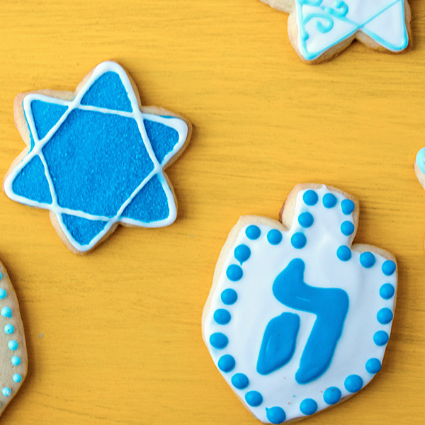Hanukkah sugar cookies decorated in blue and white and in the shapes of the Star of David and a dreidel.