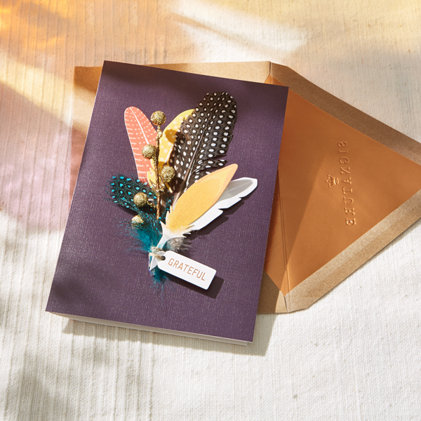A Thanksgiving card with a dark purple cover and cut paper feathers embellishing the front.