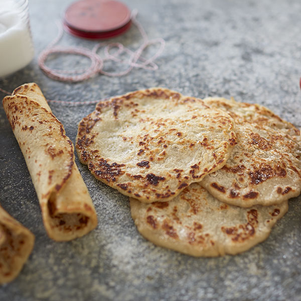 Lefse with colored spots on a counter, one rolled with cinnamon and sugar and the others lying flat.