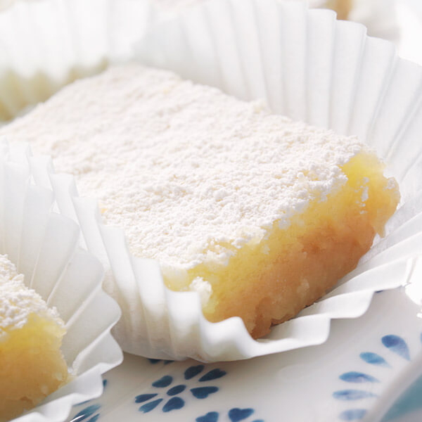Lemon bar in a cupcake liner dusted heavily with powdered sugar.