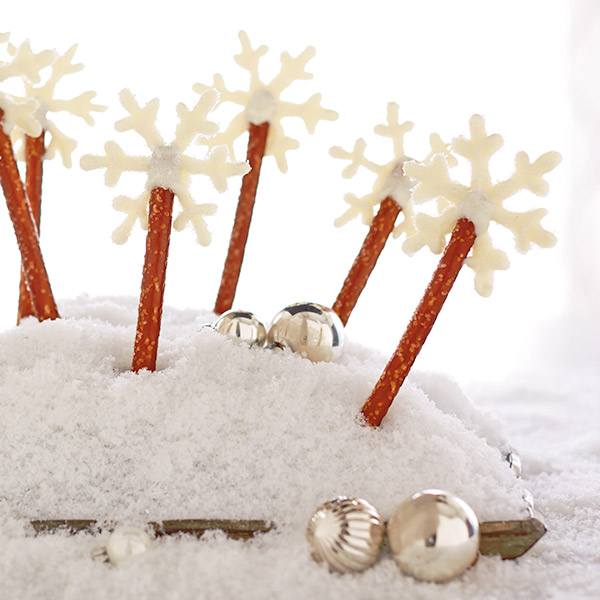 Pretzel rods with white snowflake toppers made of almond bark.