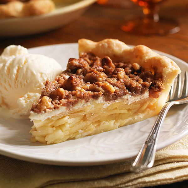 Wedge of apple pie with crispy streusel topping and a side of sour cream topping.