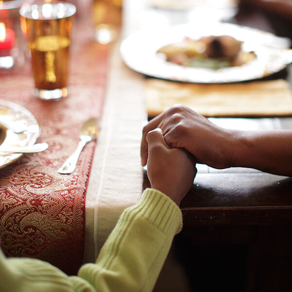 Two people holding hands at a Thanksgiving dinner table.
