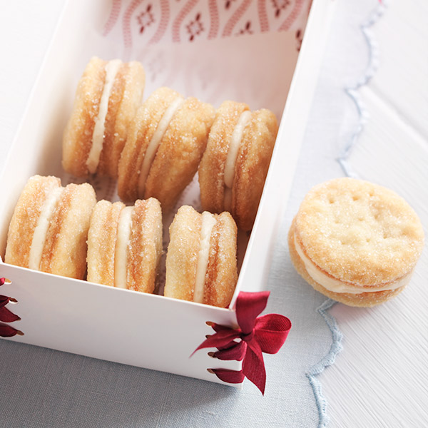 Two crisp wafer cookies sandwiched together with a creamy, buttery filling and placed neatly inside a treat box.