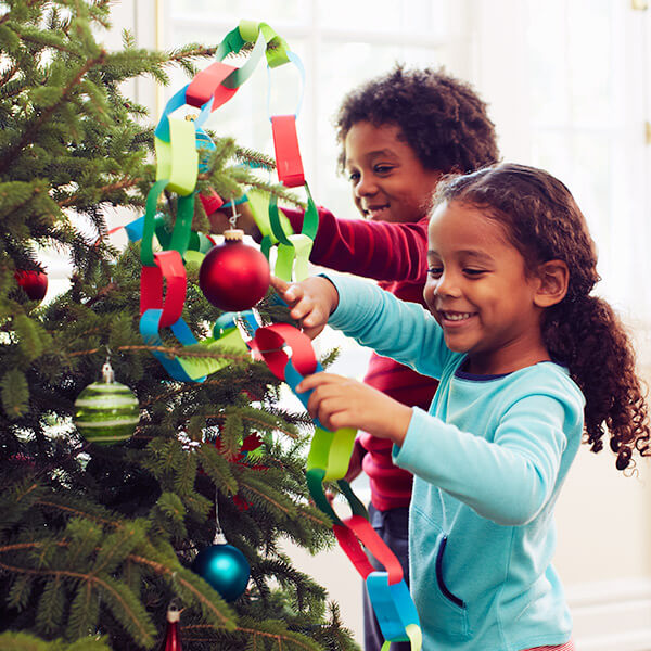 Two young girls hanging ornaments on a Christmas tree.