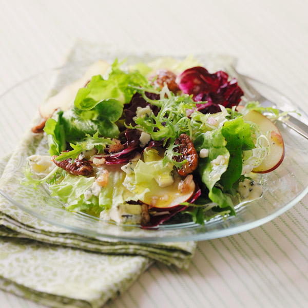 Winter apple pecan salad with various greens, apple wedges, crumbled blue cheese and sugar-coated pecans.