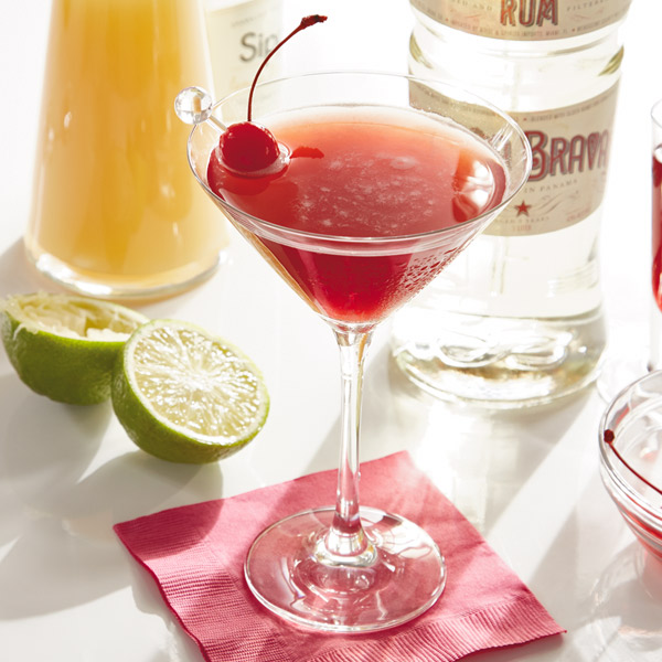 Pink rum drink with a ruby hue, served in a martini glass and garnished with a maraschino cherry.