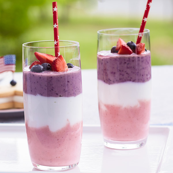 Firecracker layered fruit smoothies with a strawberry bottom layer, vanilla Greek yogurt middle layer and blueberry top layer, garnished with mixed berries.