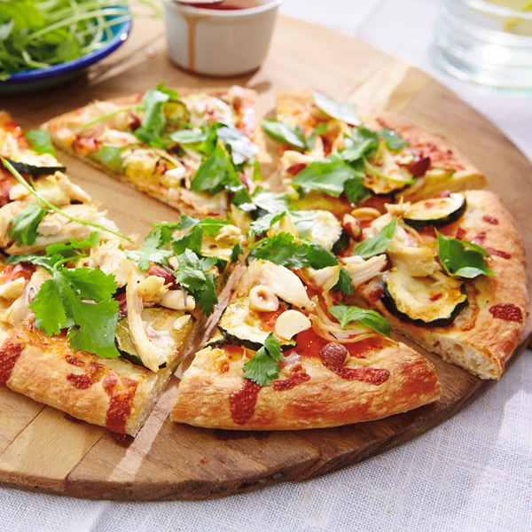 Thai chicken pizza cut into slices with zucchini, sweet Asian chili sauce drizzle, cilantro and basil.