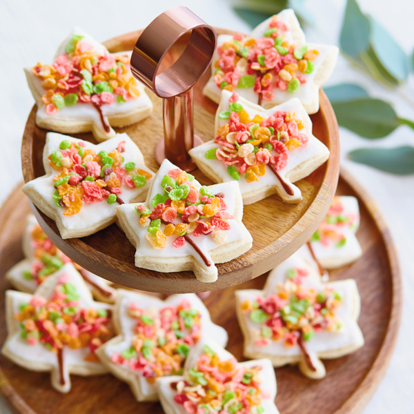 Fall sugar cookies shaped like a leaf, covered in white royal icing and garnished with green, red, orange and yellow colored rice cereal.