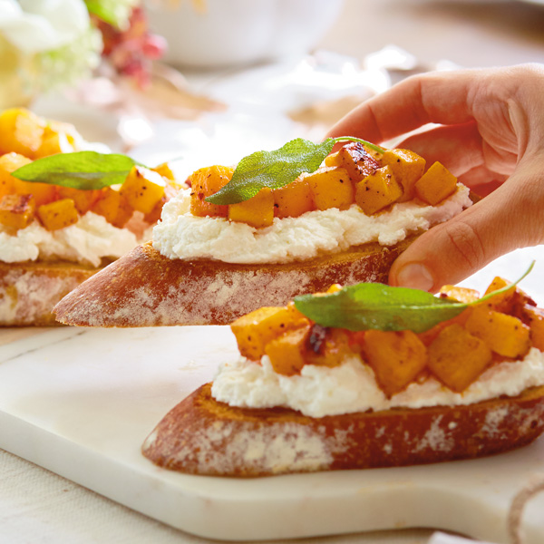 Ricotta crostini with toasted bread, creamy ricotta, roasted butternut squash and a sage leaf garnish.