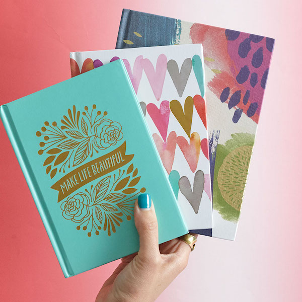 A hand holding three journals.