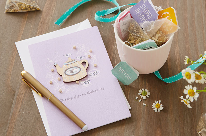 A greeting card and pen next to teabags for a Mother's Day tea party.