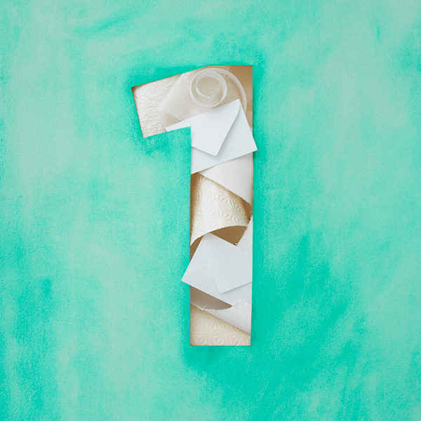 First anniversary ideas. Outline of the number 1 (for 1st anniversary) filled pieces of paper (for the traditional 1st anniversary gift) against a turquoise background