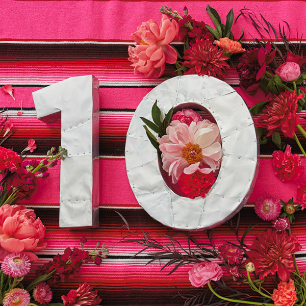 10-anniv-ideas A number ten (for 10th anniversary) made of hammered tin (a traditional 10th anniversary gift) against a pink striped background and surrounded by pink and red roses