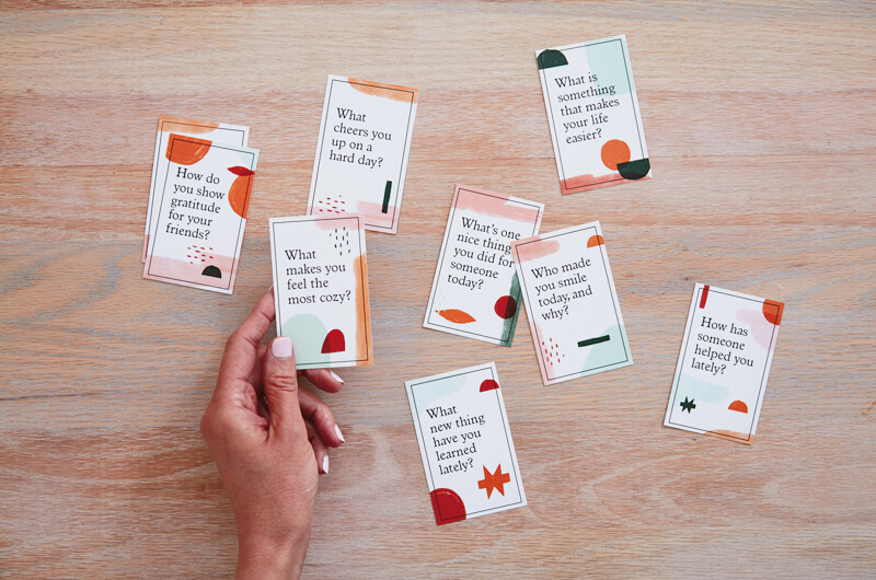 Hand holding gratitude conversation starter cards on table