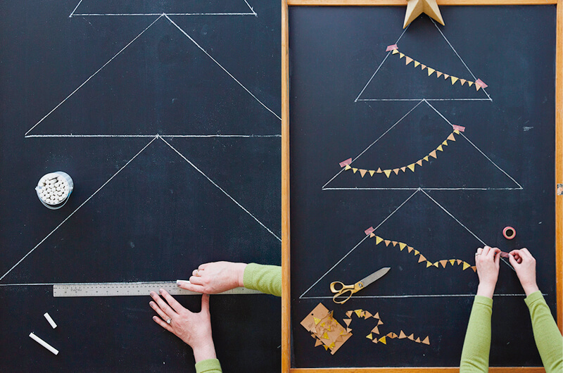 Hands drawing a Christmas tree on a chalkboard and decorating it with mini garland.