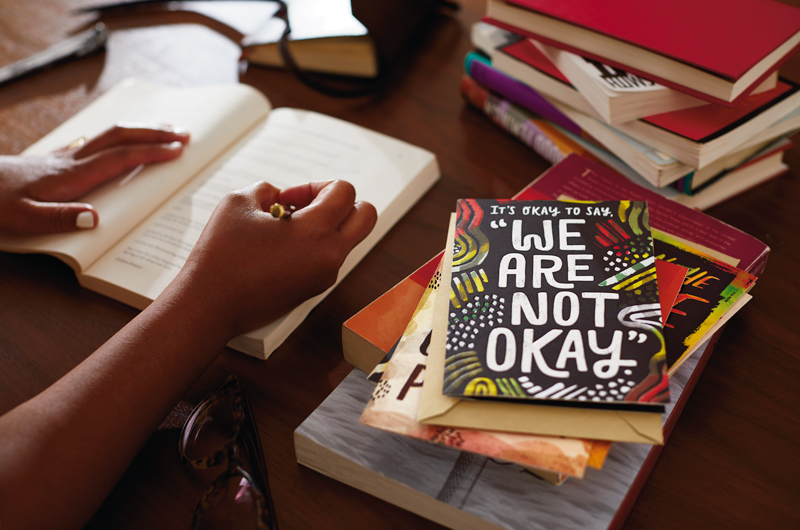 Hand writing with card that says “It’s okay to say, ‘We are not okay.’”