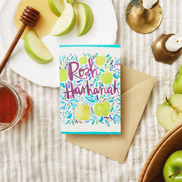 Rosh Hashanah Card on a table with apples, honey and candles