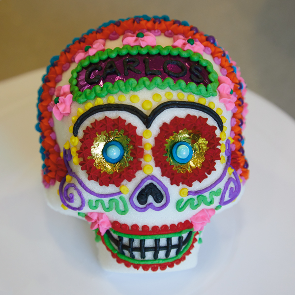 Front view of decorated sugar skull with gold foil eyes and royal icing embellishments in red, pink, green, blue and purple.