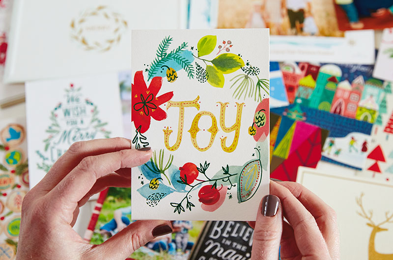 Hands holding a Christmas card with JOY on the cover.