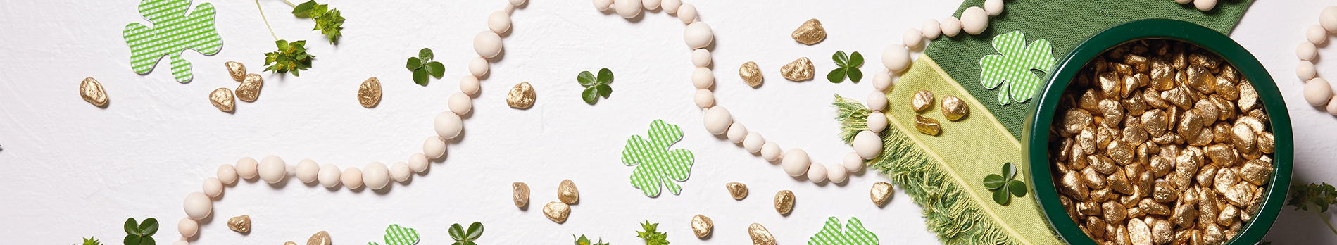 St. Patrick's Day background with a green bowl filled with gold nuggets, shamrock cutouts and a green table runner.