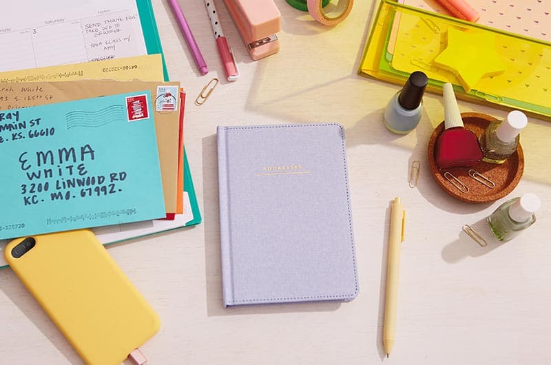 Address book with chambray cover on desktop with envelopes, phone case and office accessories