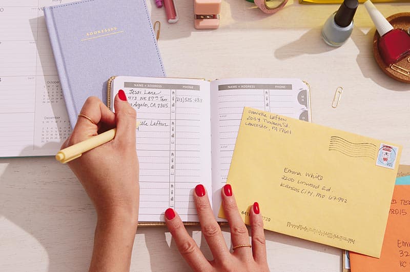Hands updating address book with postmarked envelope nearby