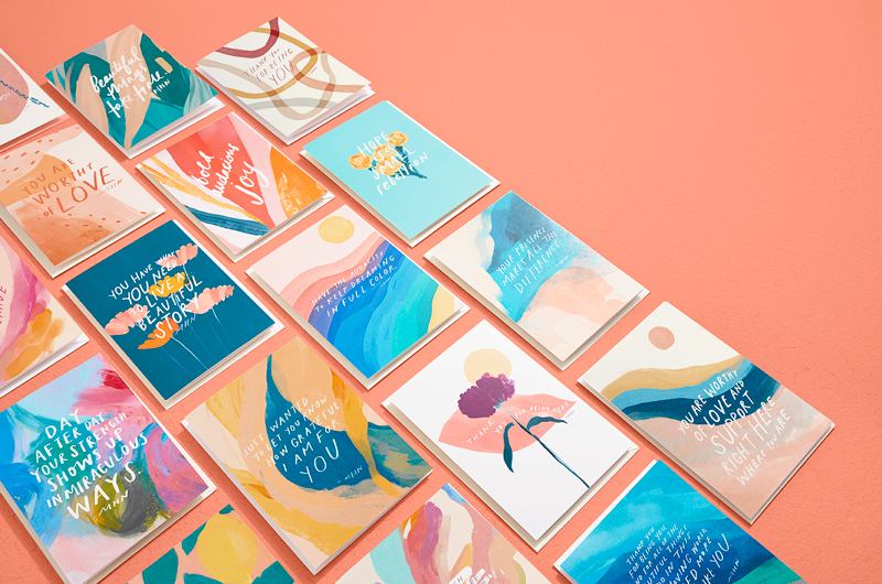 Various cards from the Morgan Harper Nichols Real Stories Collection laid flat on a bright melon-colored surface.