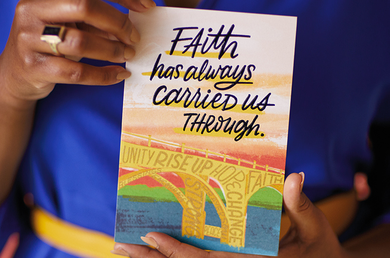 Hands holding an Uplifted and Empowered card that pictures a bridge and reads,