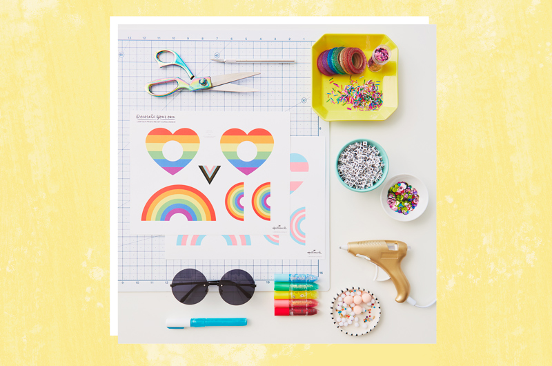 Craft supplies needed to make DIY Pride Month sunglasses, including free printable, a hot glue gun, beads, wire, scissors and moms.