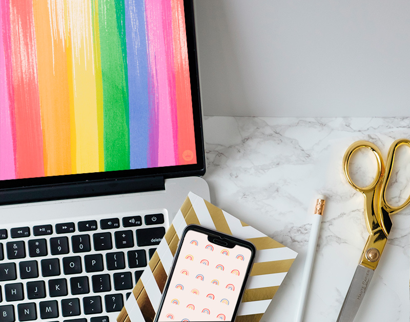 A laptop and a smartphone displaying free downloadable Pride Month wallpapers from Hallmark.