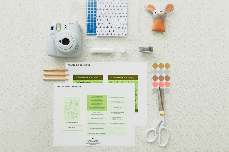 The suggested content of Hannah's DIY Travel Games kit, including free printables, dot stickers, Washi tape, pencils, a small journal, a stuffed animal, a glue stick and an instant camera.
