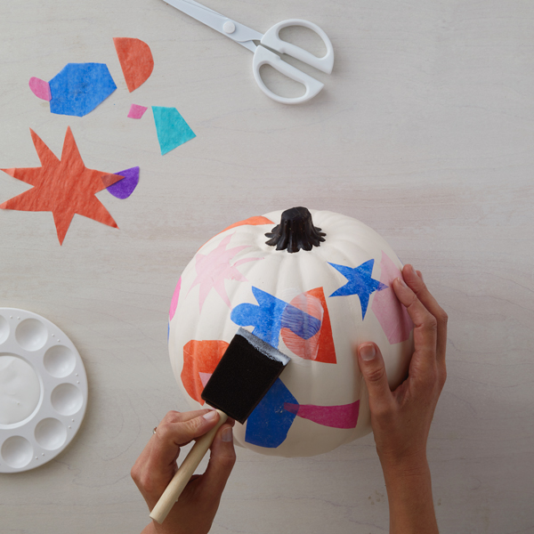 Hands coating the finished decoupage pumpkin with a final coat of Mod Podge.