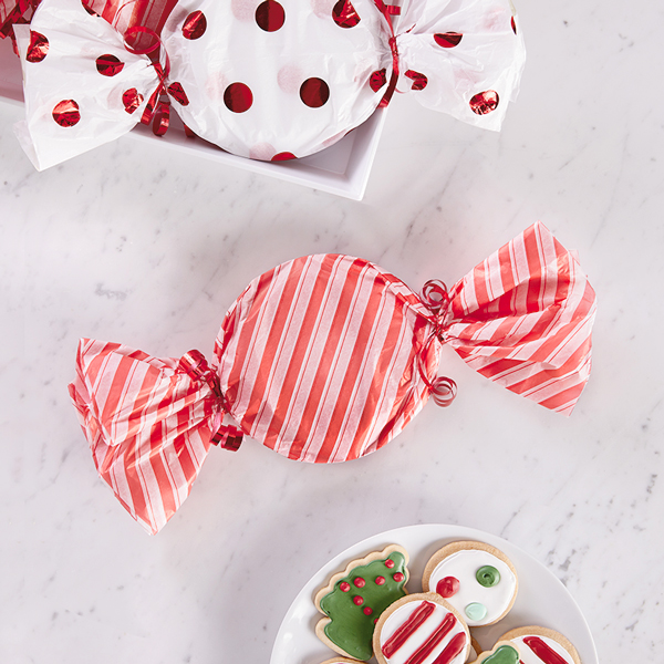 A plate of Christmas cookies wrapped up like a piece of hard candy, with curled ribbon tied on its ends.