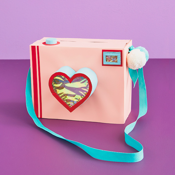 A valentine box shaped like a camera with a strap and a heart shaped lens.