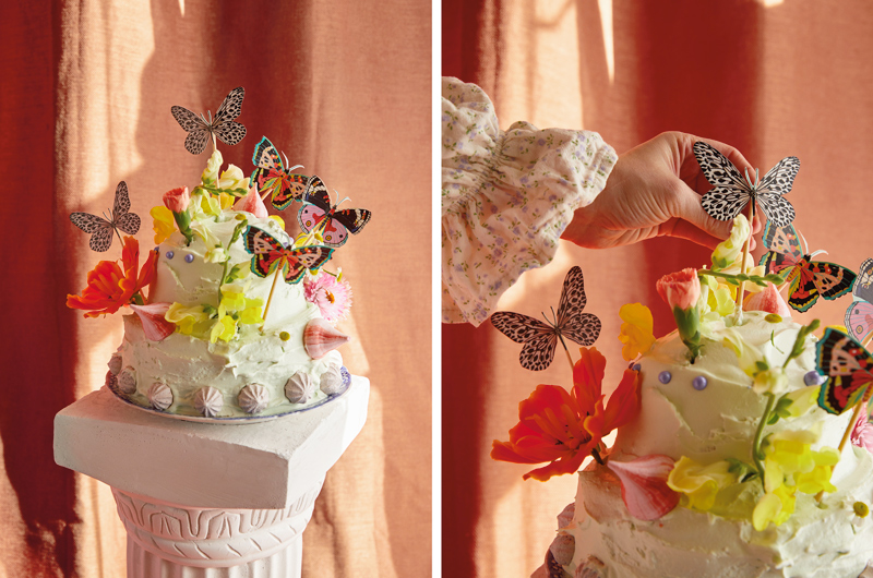 A cake decorated with meringues, edible pearls and edible flowers, and a DIY butterfly cake topper sit atop a cake stand that looks like a Roman column.
