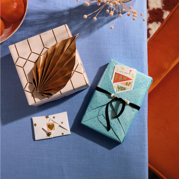 Three gifts wrapped in styles inspired by origami paper art sit on a blue damask tablecloth.