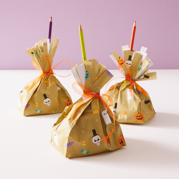 Three Halloween treat bags made to look like witches' brooms sit on a white surface in front of a pale purple background.