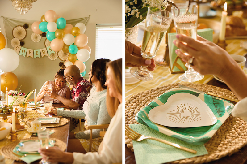 The guests at an anniversary party sit at a long, rectangular table set with Celebrate! partyware, rattan placemats, and vintage glassware, with the guests of honor seated at the far end; next to this is a closeup of two hands holding up vintage glassware filled with champagne to toast while a Celebrate! place setting sits beneath.