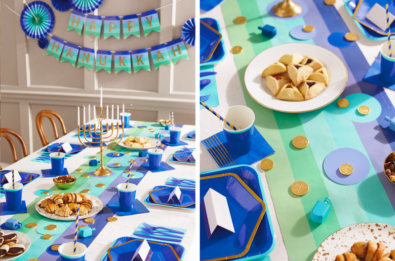 A Hanukkah tablescape featuring Hallmark Celebrate! partyware in shades of blue, like bright blue hexagonal plates with gold rims, matching bright blue cocktail napkins with gold foil accents, a table runner in a cool blue ombre stripe pattern, and a banner hanging in the background with the message