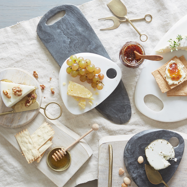 A downshot of an appetizer table featuring different cheeses, fruit and spreads.