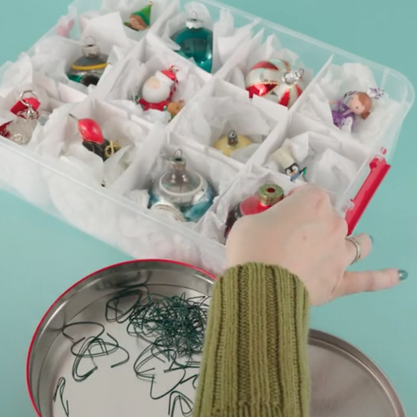 A woman reaches to place a vintage ornament into an ornament storage box with separate compartments for each ornament that are cushioned with tissue paper.