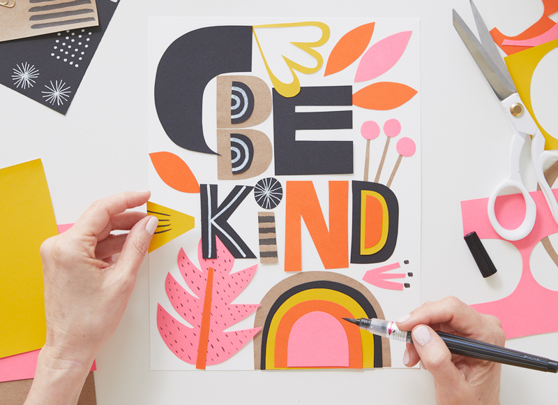 A woman's hands piece together a paper collage poster that reads,