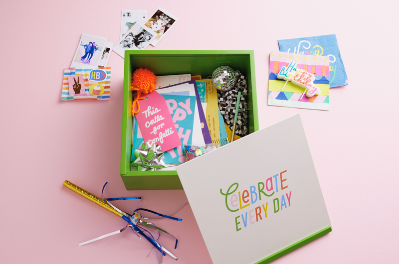 A birthday memory box sits on a light pink surface; the box is lime green and has a white lid that reads,