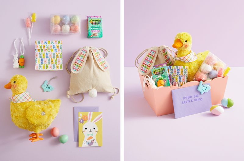 A selection of gifts for a kid's Easter basket, including a plush, interactive, egg-laying duck; a drawstring canvas bag with bunny ears and a puffy bunny tail; a treat bag covered in a repeating pastel bunny print; a Better Together ornament set featuring a white bunny and a carrot; a handmade bunny name tag; a pack of Crayola Colors of Kindness crayons; and a pack of pastel, egg-shaped sidewalk chalks.