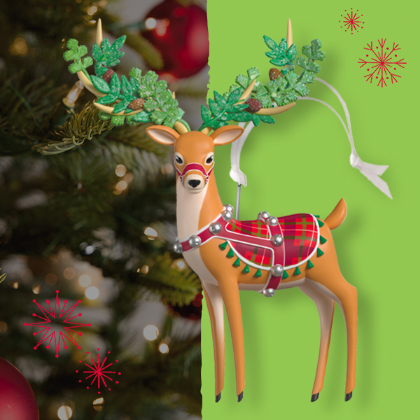 A Keepsake Ornament portraying a graceful reindeer decked out in a red and green plaid blanket, a red harness with silver jingle bells, and evergreen boughs woven in its antlers.