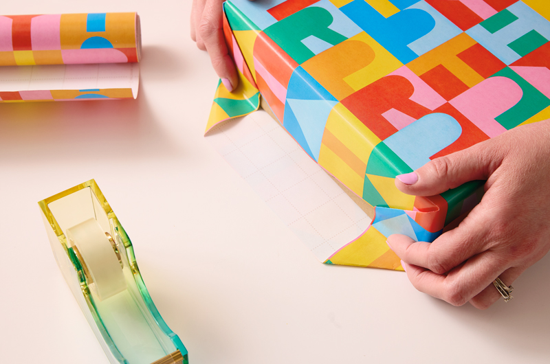 A woman's hands creases corners into the edges of a present that she is wrapping.