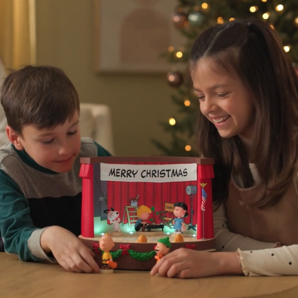 Two young children—a boy of around 6 and a girl of around 8—are smiling down at an interactive tabletop decoration featuring a scene from the animated Christmas classic, 